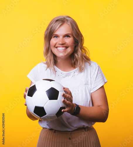 Portrait of cheerful woman holding soccer ball while standing over yellow background © Vulp