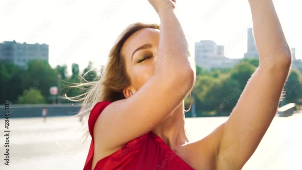 portrait of attractive blonde woman dancing on windy street with lens flare