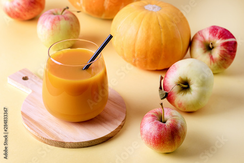 Glass of Fresh Tasty Pumpkin Juce with Black Strew on Wooden Cutting Board Ripe Apples and Pumpkin on Yellow Background Horizontal