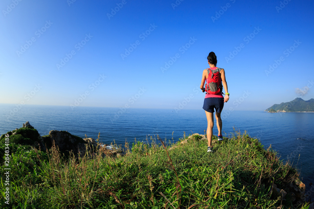 Young fitness woman running on seaside mountain trail
