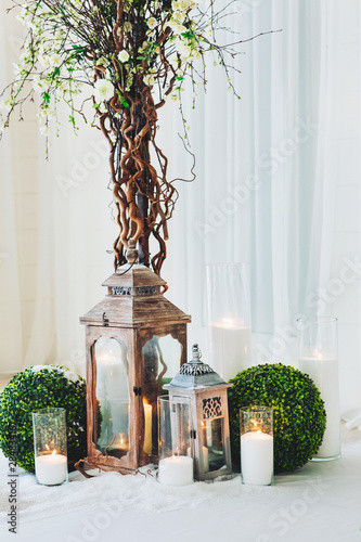 Indoor wedding ceremony with white wedding arch decorated with flowers and big white candles photo