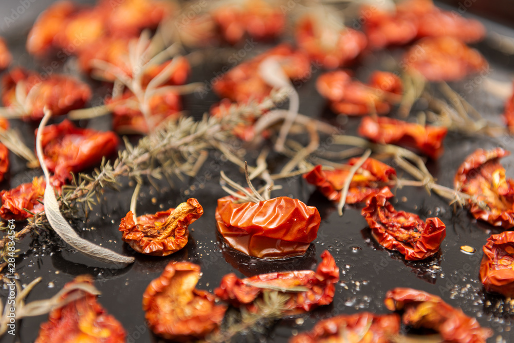 Dried tomatoes on black tray with herbs