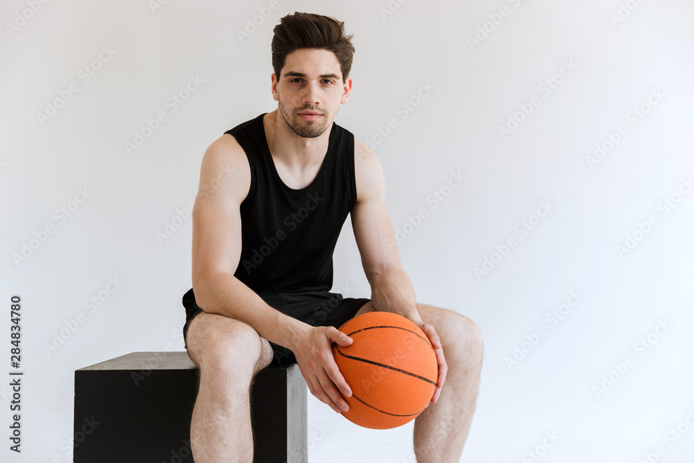 Concentrated serious strong young sports man basketball player holding ball isolated over white background. Concentrated serious strong young sports man basketball player holding ball isolated over white background.