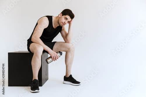 Handsome tired strong young sports man drinking water isolated over white background.
