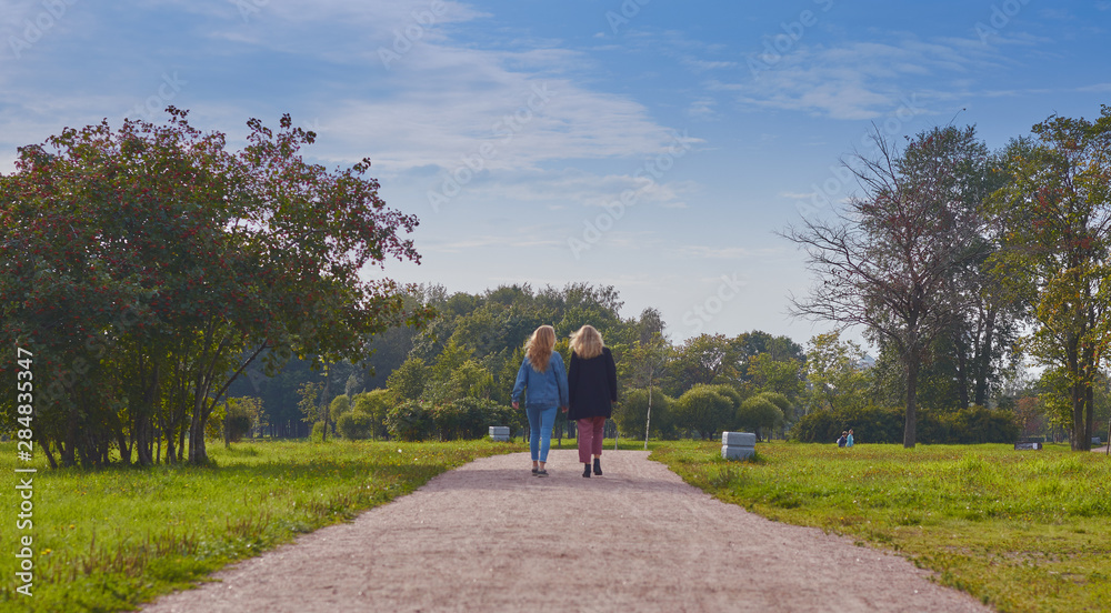 Rear view of two girls friends walking together in a park in warm, clear weather. walk in nature.