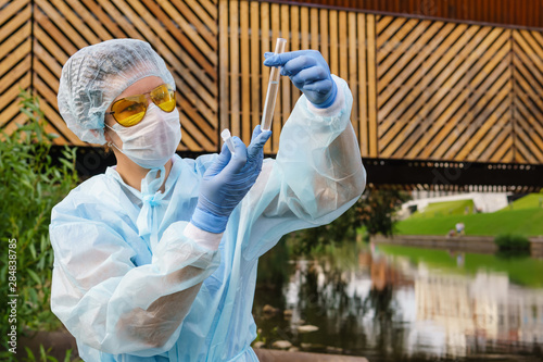 female ecologist or epidemiologist checks water quality in urban pond photo