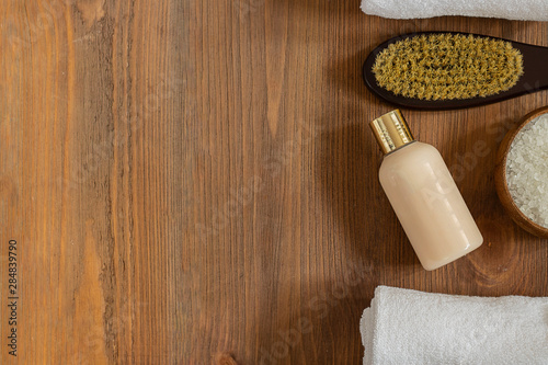 woman body and skincare, bath and spa products, sea salt in bowl, mochup bottle, white towel, dry massage brush on brown wooden background. Beauty, cosmetics. Horizontal with copy space. Top view photo