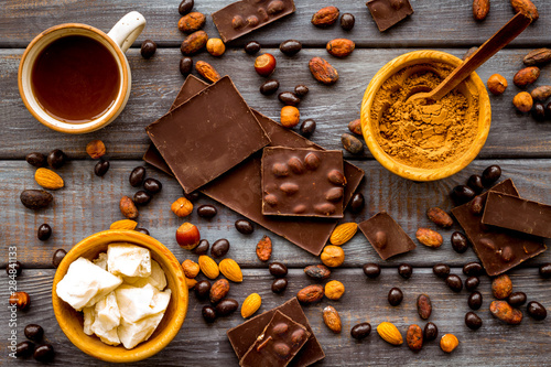 Tea with homemade chocolate bars, nuts, coffee beans on wooden background top view