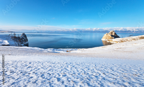 Baikal Lake in a sunny December morning after a snowfall. View of the Khuzhir Bay, Cape Burhan and the Shamanka Rock. Beautiful winter landscape