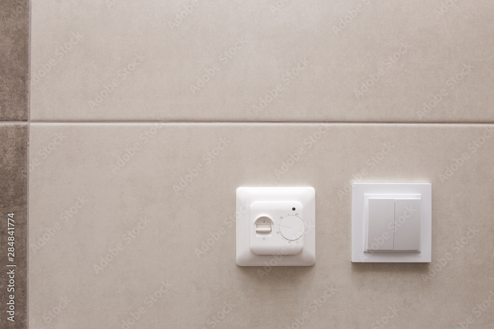 White temperature controller of a warm floor on a gray wall. White temperature controller of a warm floor on a gray wall.