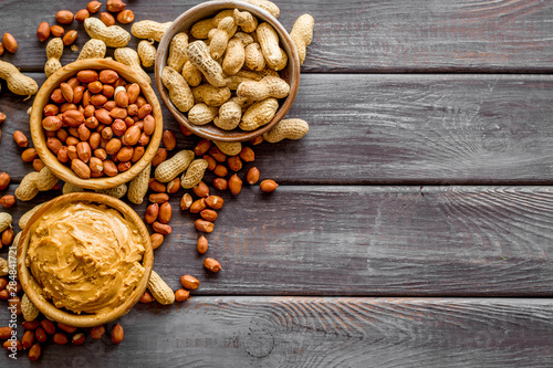 Product for hearty breakfast with peanut butter in bowl near nuts on wooden background top view mockup