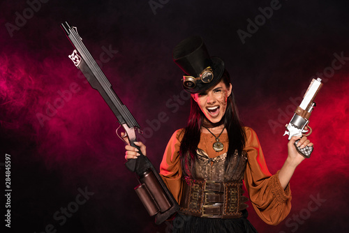 front view of screaming steampunk woman holding gun and pistol in pink smoke on black © LIGHTFIELD STUDIOS