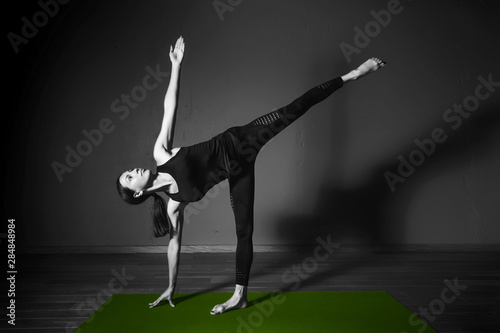 Black white photo of Young beautiful woman brunette in black clothes practice yoga ardha chandrasana in dark studio green mat Sport meditation monochrome photo