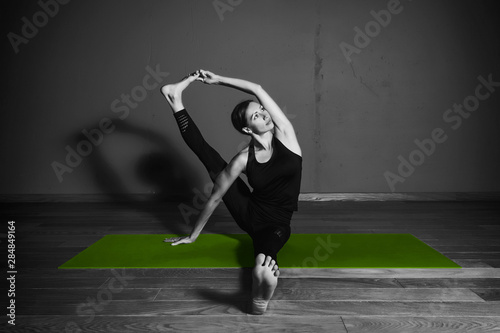 Black white photo of Young beautiful woman brunette in black clothes practice yoga in dark studio green mat Sport meditation monochrome