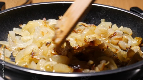 Chopped onions fried  in hot frying pan, hand mixing with wooden spoon spatula. Vegetable preparing, meals with vegetables. Slow motion