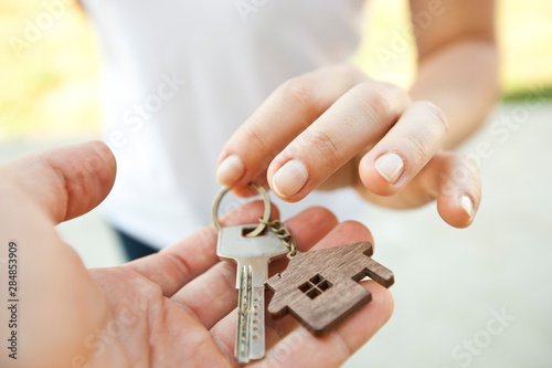 Man giving the metal key from door with wooden trinket in shape of house to the woman