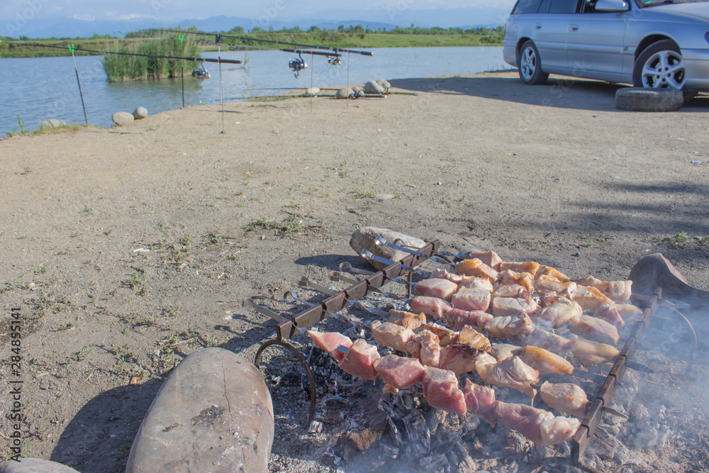 Obraz premium Meat on skewers fried on the grill in the open air, visible hands of the cook. Fishing adventures, relaxation, picnic