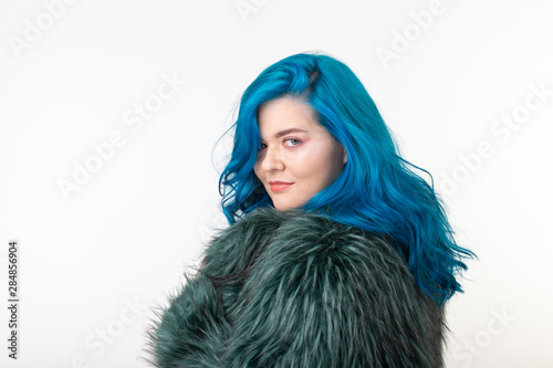 Animal protection, fashion and hair concept - beautiful girl with blue hair dressed in artificial fur coat standing on white background with copy space