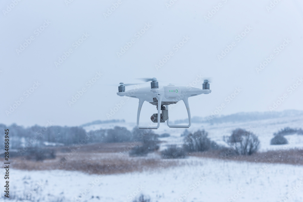 Hovering drone taking pictures of wild nature. Cold winter weather. Cloudy day with falling snow Hovering drone taking pictures of wild nature. Cold winter weather. Cloudy day with falling snow