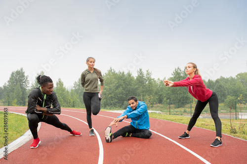 Young healthy intercultural men and women in sportswear doing physical exercises