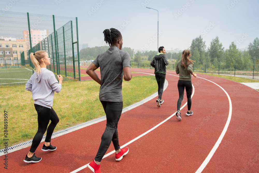 Fototapeta premium Rear view of young intercultural people in activewear running down race track