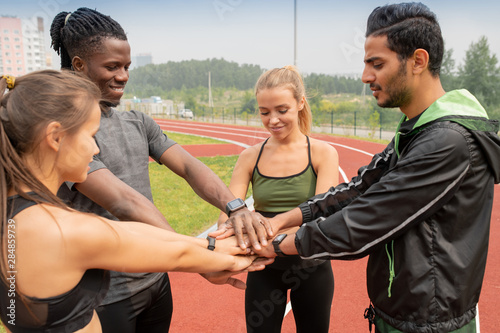 Four young intercultural people in activewear making pile of hands outdoors