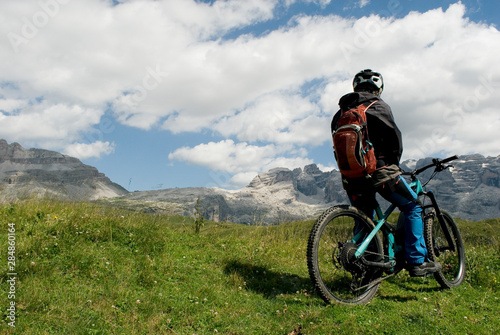 man with electric bike, e-bike, ebike, looking mountains of Brenta Peak, Grostè Pass, meadow, Dolomites, Madonna di Campiglio, summer, sport, adventure, travel, Alps, Trentino Alto Adige, Italy