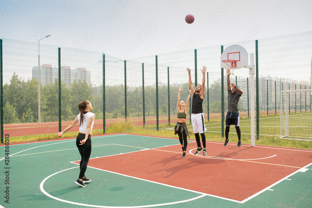 Team of young intercultural friends or students working out on basketball court