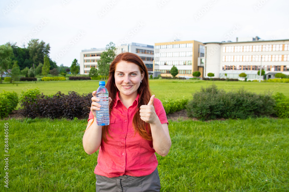 Young girl in bright summer clothes holds a plastic bottle of water on the background of the park Young girl in bright summer clothes holds a plastic bottle of water on the background of the park