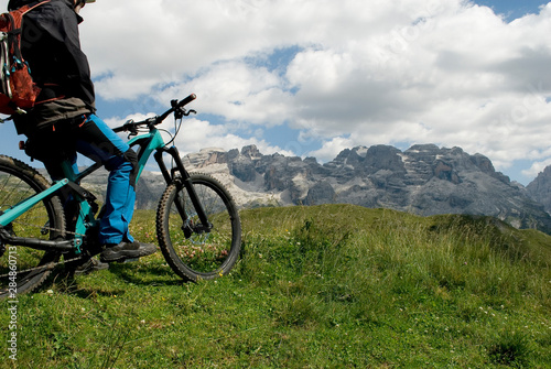 man with electric bike, e-bike, ebike, looking mountains of Brenta Peak, Grostè Pass, meadow, Dolomites, Madonna di Campiglio, summer, sport, adventure, travel, Alps, Trentino Alto Adige, Italy
