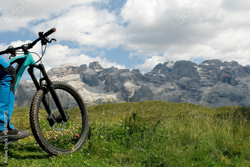 man with electric bike, e-bike, ebike, looking mountains of Brenta Peak, Grostè Pass, meadow, Dolomites, Madonna di Campiglio, summer, sport, adventure, travel, Alps, Trentino Alto Adige, Italy