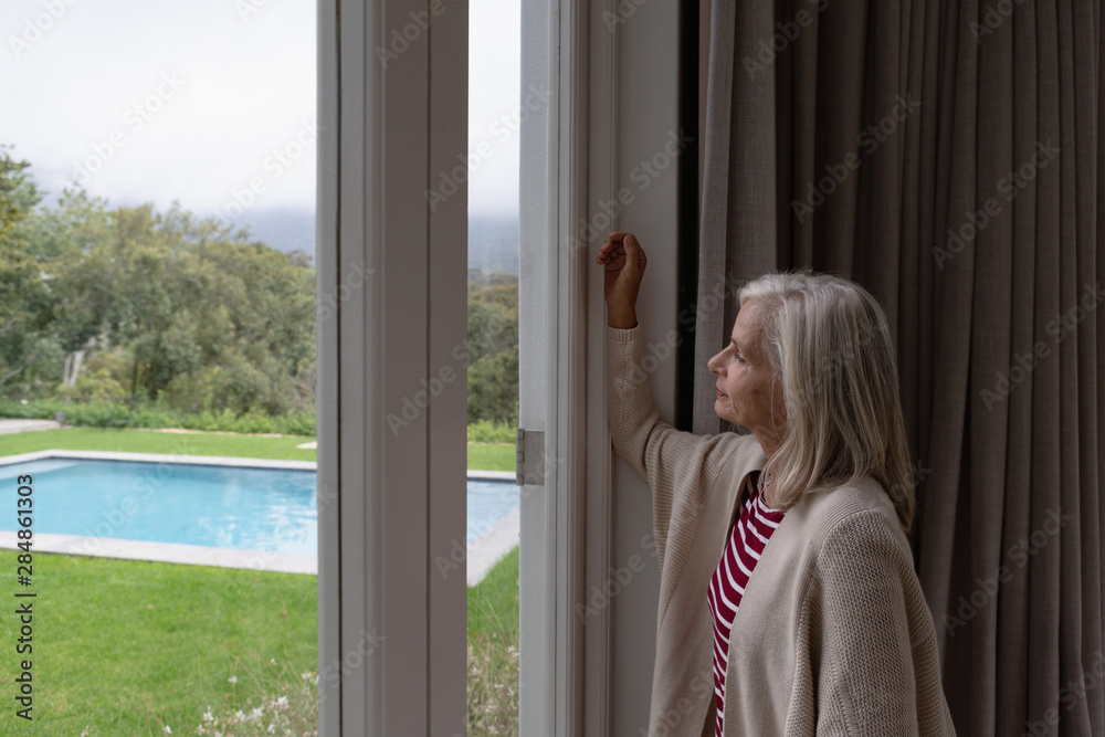 Active senior woman looking through window in a comfortable home Active senior woman looking through window in a comfortable home