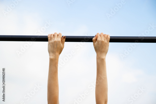 Girl passes the standards for pulling up on a horizontal bar in the park sunny day.