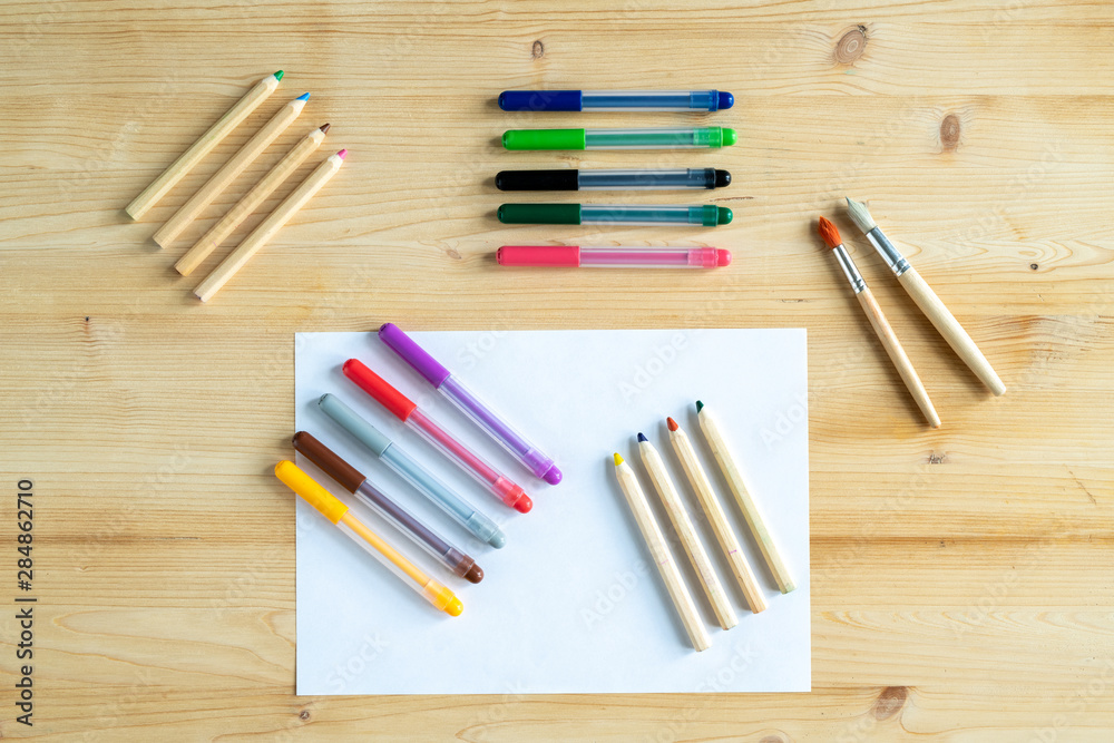 Obraz premium View of blank paper and several sets of crayons and pens and two paintbrushes
