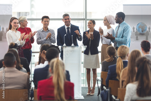 Businessman standing at podium with colleagues and speaks in a business seminar © WavebreakMediaMicro