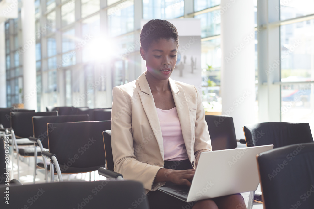 Businesswoman sitting on chair and using laptop in lobby Businesswoman sitting on chair and using laptop in lobby