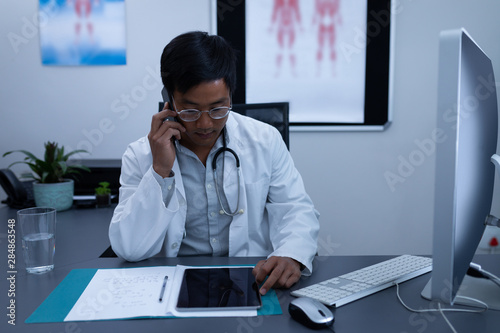 Doctor talking on mobile phone while using digital tablet