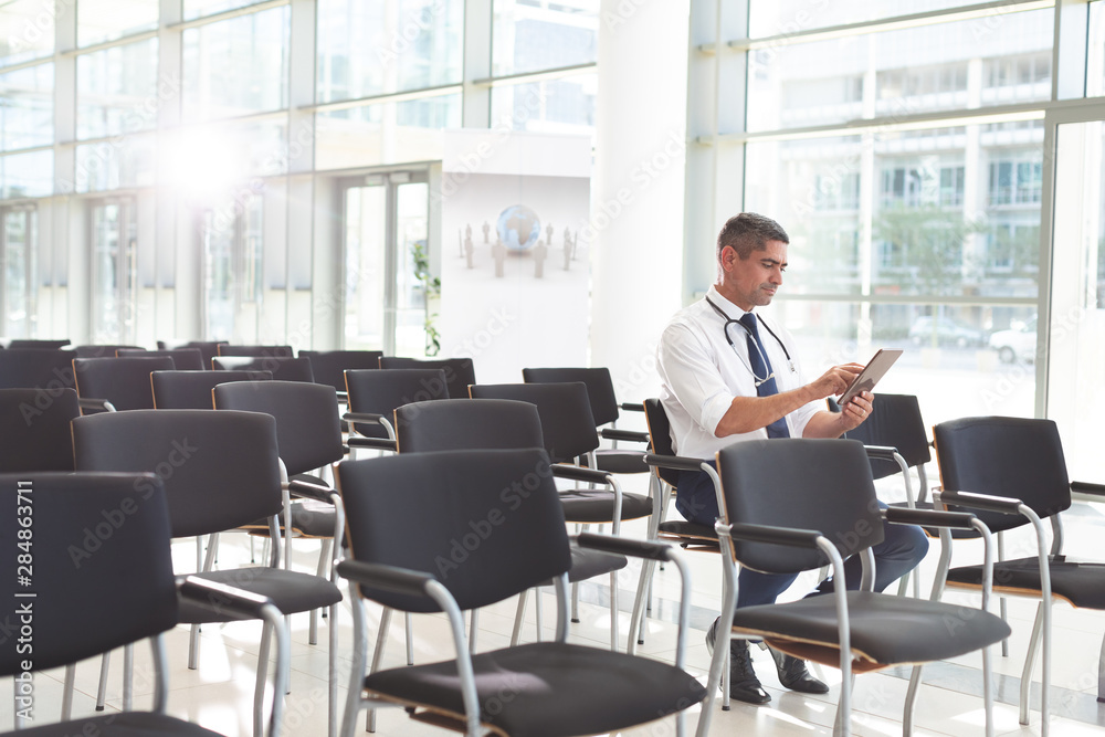 Male doctor sitting on chair and using digital tablet in a conference room Male doctor sitting on chair and using digital tablet in a conference room
