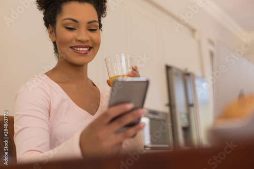 Woman having orange juice while using mobile phone at home