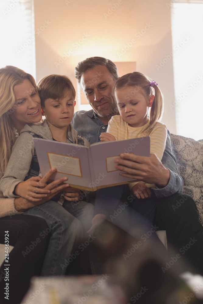 © wavebreak3 - Family reading story book in living room