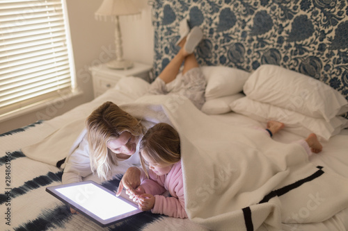 Mother and daughter using digital tablet in bedroom