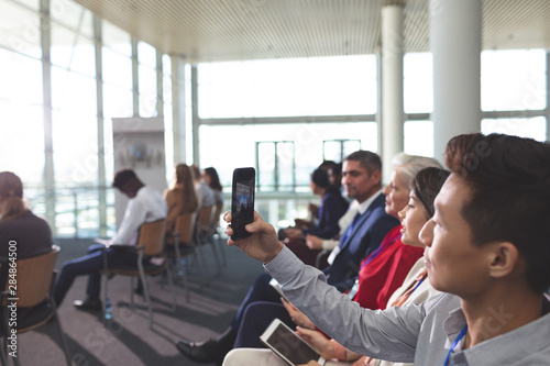 Young businessman clicking photo with mobile phone in a business seminar