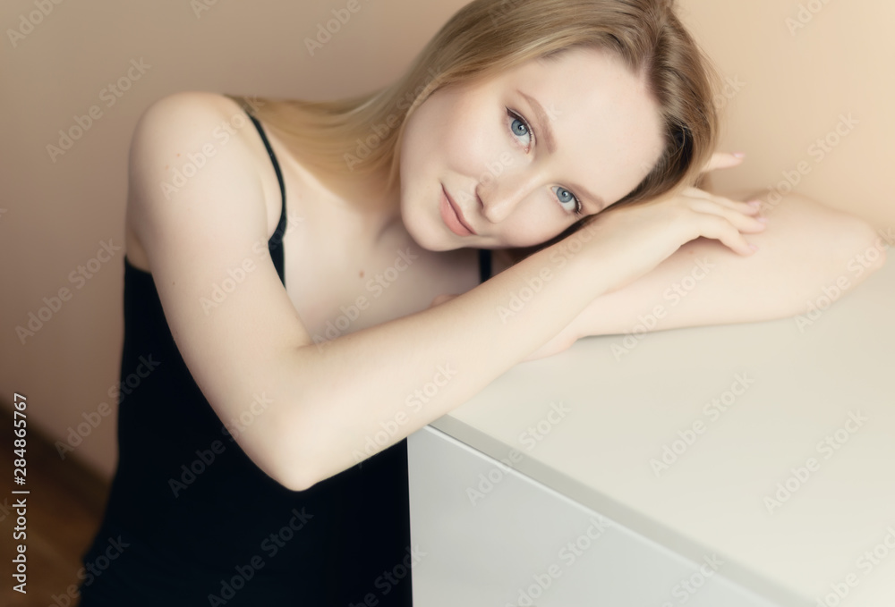 Graceful young woman in a black top posing against beige wall. Graceful young woman in a black top posing against beige wall.
