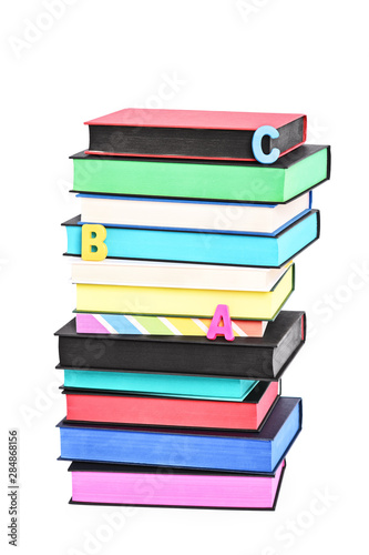 Stack of colorful books witch different sprayed edges and scattered letters spelling ABC, isolated on white background.