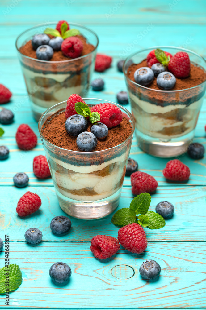 Classic tiramisu dessert with blueberries and strawberries in a glass cup on wooden background Classic tiramisu dessert with blueberries and strawberries in a glass cup on wooden background