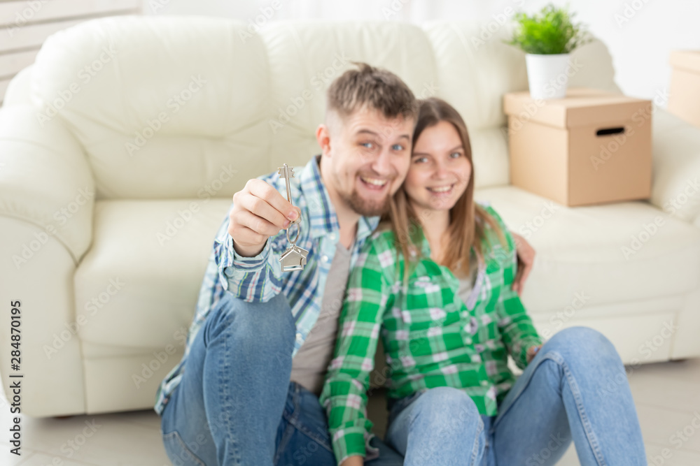Young positive couple holding keys to a new apartment while standing in their living room. Housewarming and family mortgage concept.