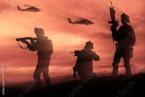 Three military soldiers silhouettes on sunset sky background.
