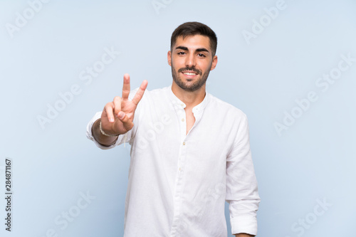 Handsome man with beard over isolated blue background smiling and showing victory sign © luismolinero