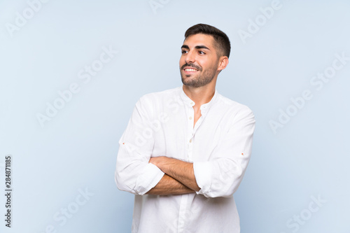 Handsome man with beard over isolated blue background looking up while smiling