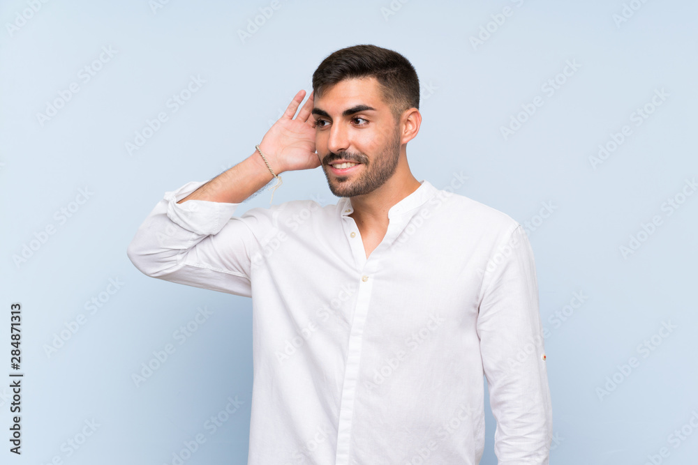 Handsome man with beard over isolated blue background listening to something by putting hand on the ear Handsome man with beard over isolated blue background listening to something by putting hand on the ear